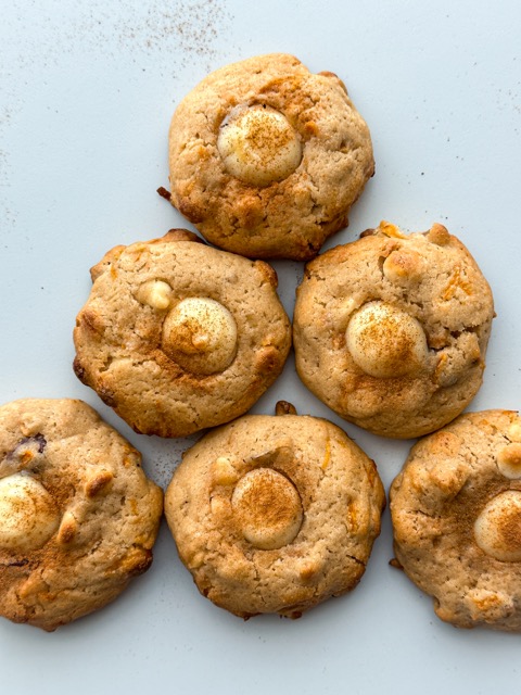 Freshly baked Carrot Cake Cookies with visible cream cheese centers, adorned with chopped walnuts and white chocolate chips, placed on a rustic wooden table.